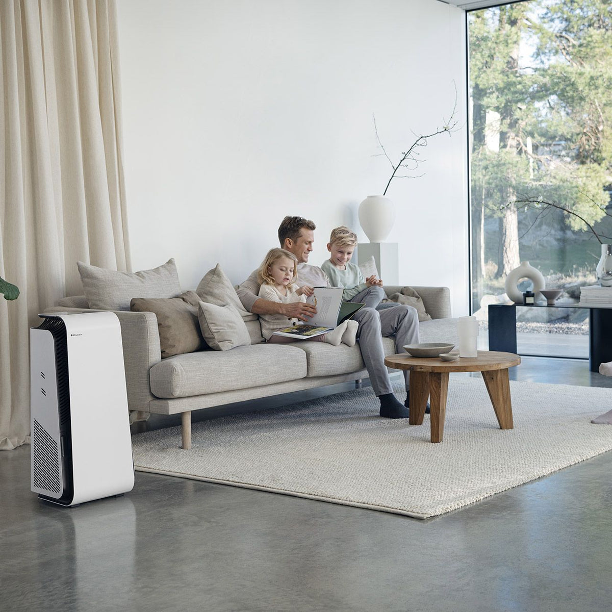 Weißer Blueair HealthProtect 7440i Luftreiniger im Wohnzimmer neben Sofa mit Vater und zwei Kindern
