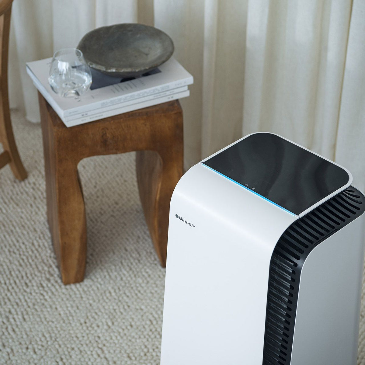 Blueair HealthProtect 7440i Luftreiniger in Weiß neben Holzhocker im Wohnraum
