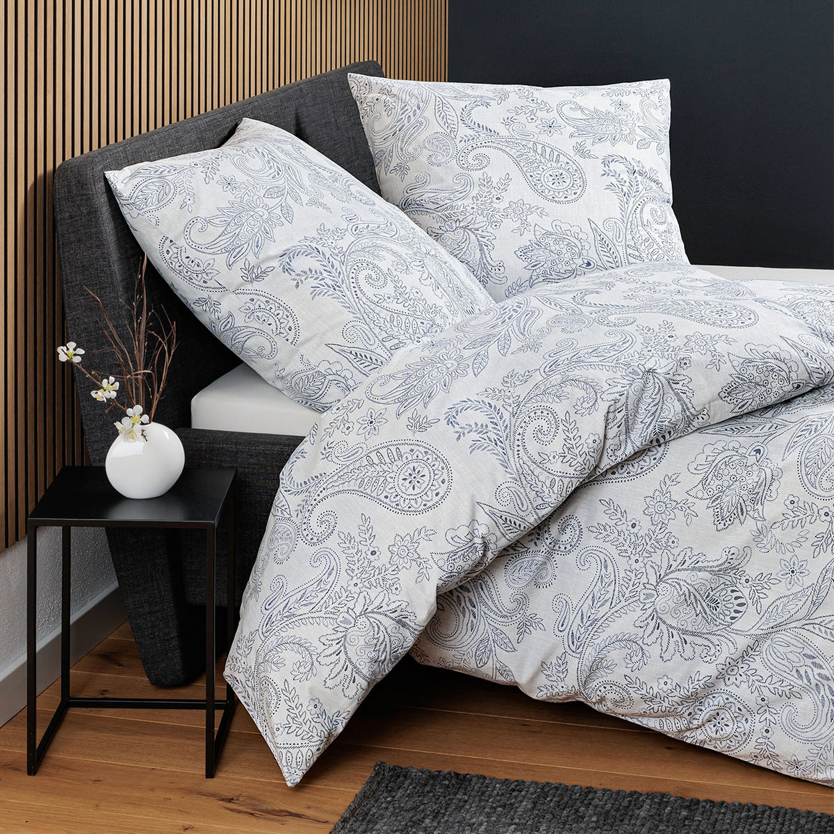 Janine Cortina Paisley Bettwäsche in Blau auf Bett mit dunklem Kopfteil, Schrägansicht im Schlafzimmer