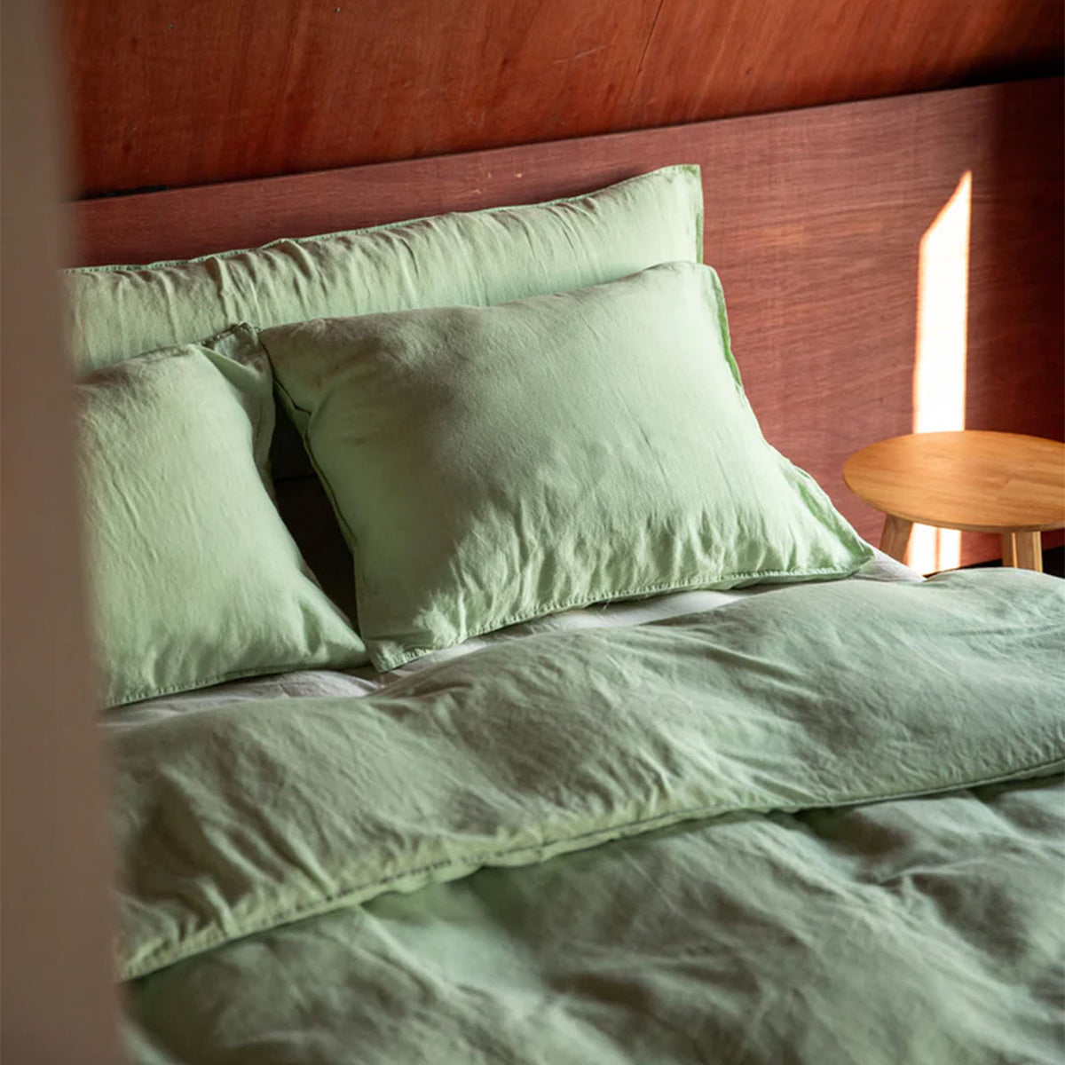 Suite702 Leinen-Mix Bettbezug in Green Mint mit Kissenbezügen auf Bett vor Holzwand