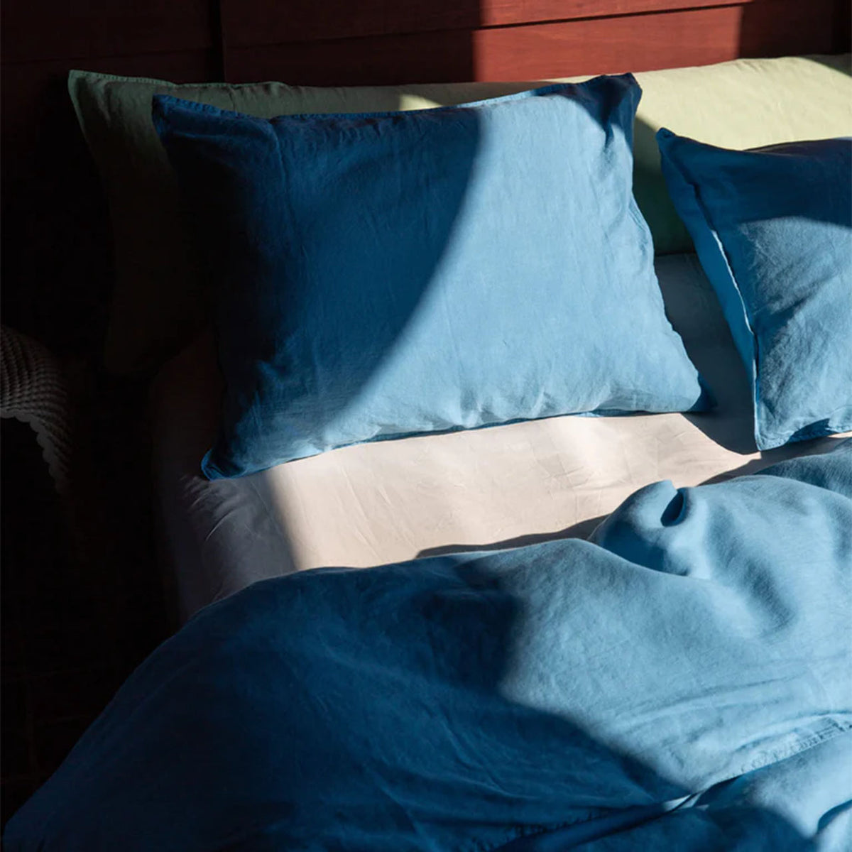 Suite702 Leinen-Mix Bettdeckenbezug in „True Blue“ mit Kissen im Sonnenlicht auf dem Bett