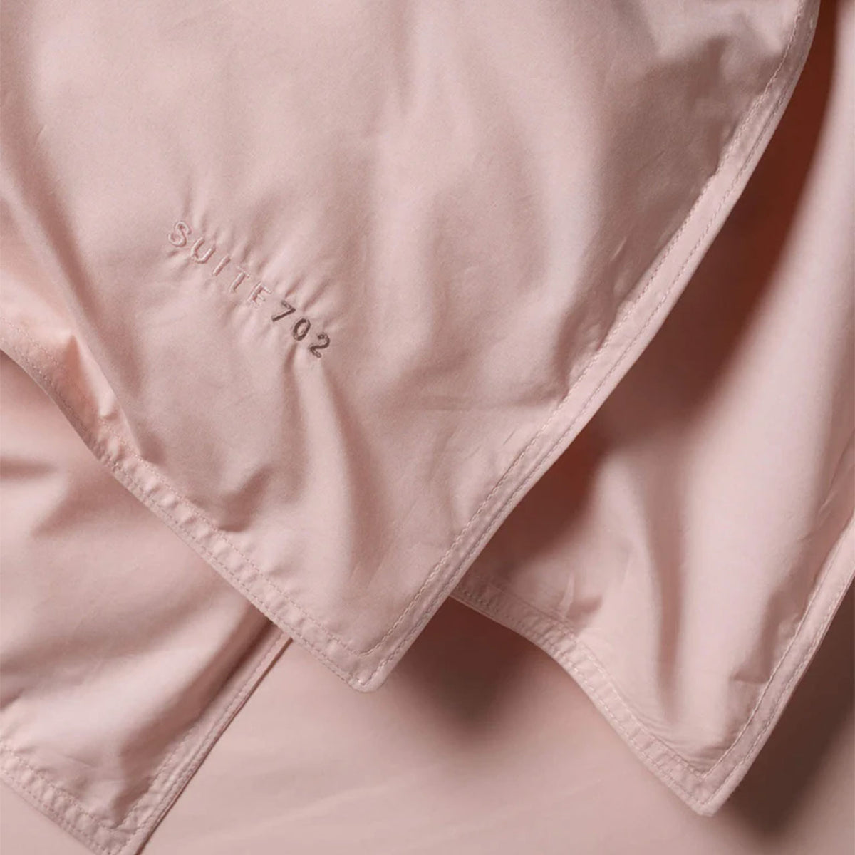 Nahaufnahme der Eckennaht des Suite702 Perkal Bettdeckenbezugs in Rosa mit Schriftzug „Suite702“