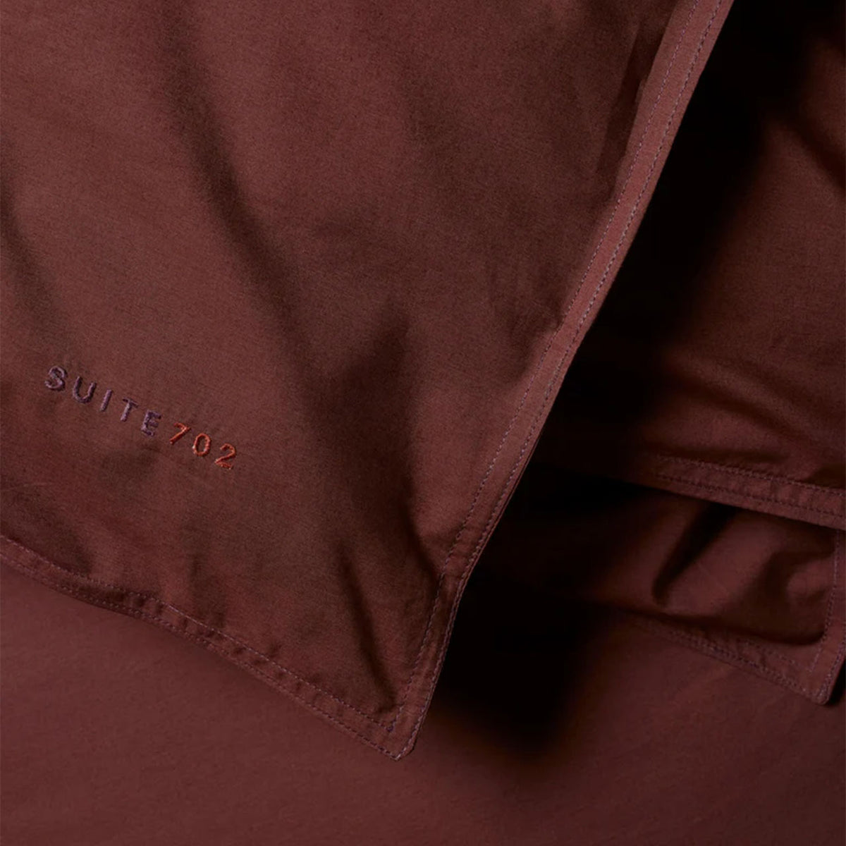 Nahaufnahme des „Suite702“-Schriftzugs auf dem Perkal Bettdeckenbezug in Coffee Brown mit Eckknopf