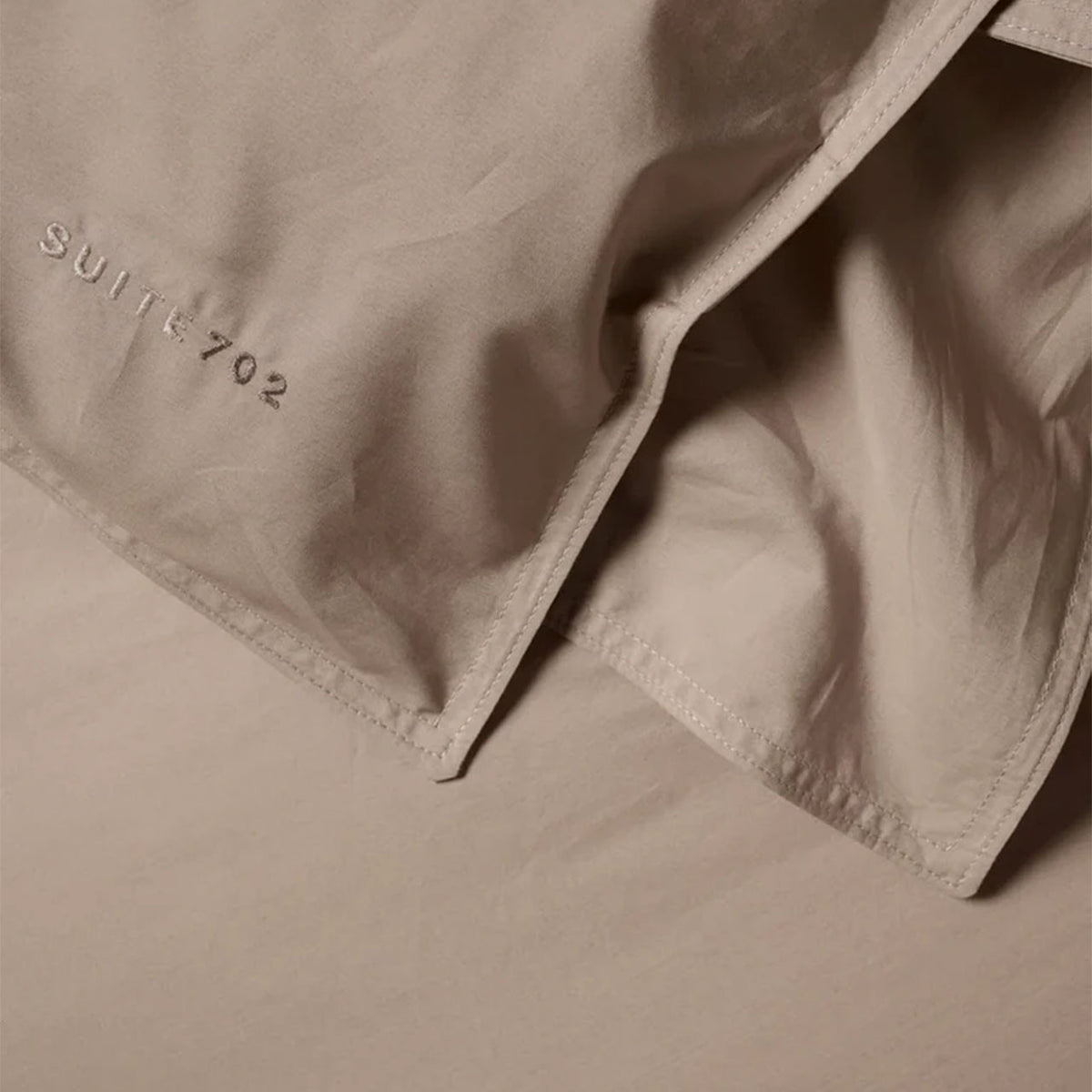 Nahaufnahme der Eckenöffnung des Suite702 Perkal Bettdeckenbezugs in Camel mit Schriftzug „Suite702“