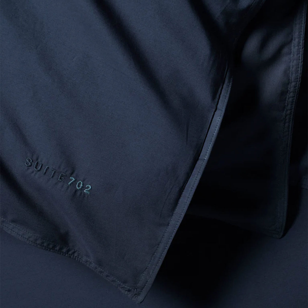 Nahaufnahme der Öffnung des Suite702 Perkal-Bettdeckenbezugs in Navy mit eingesticktem „Suite702“-Schriftzug