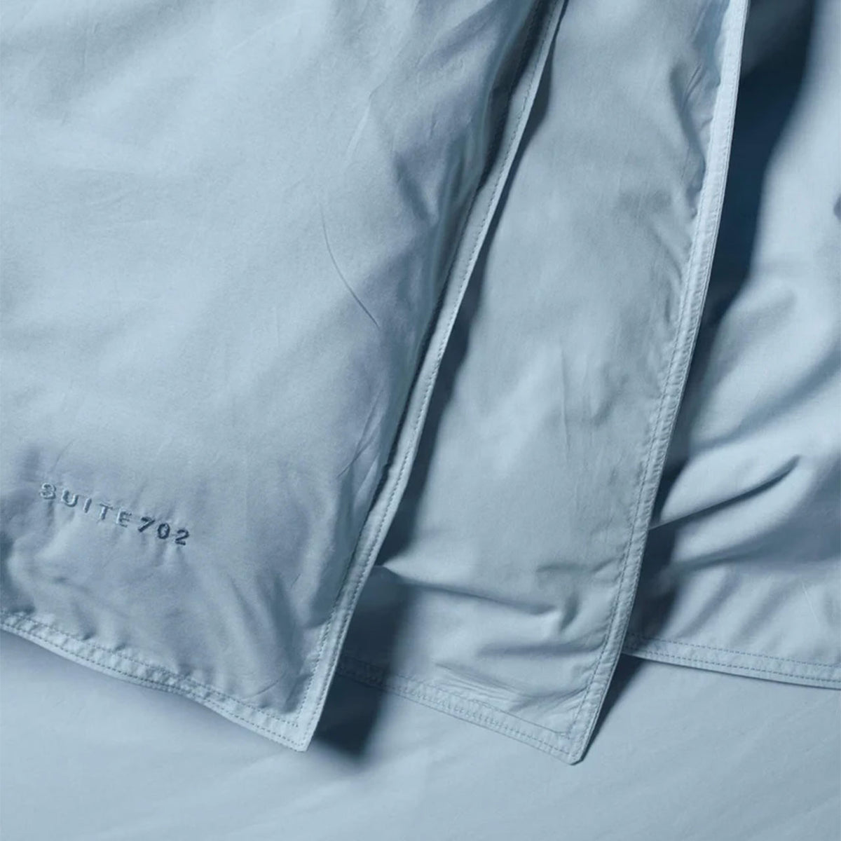 Nahaufnahme des Suite702 Perkal Bettdeckenbezugs aus Bio-Baumwolle in Sky Blue mit Schriftzug „Suite702“