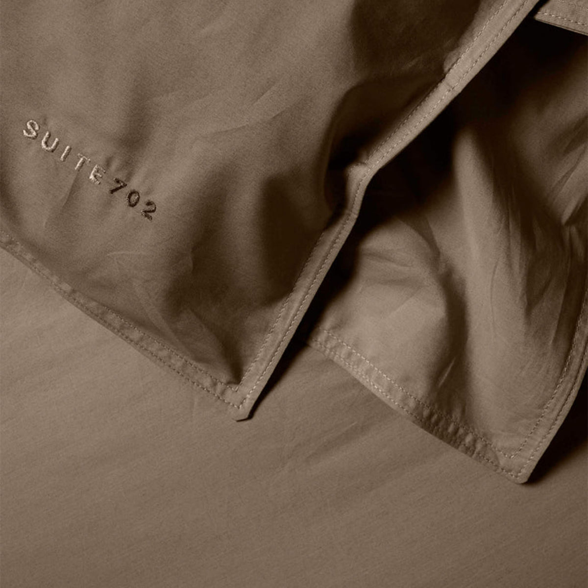 Nahaufnahme der Eckennaht des Suite702 Perkal-Bettdeckenbezugs in Smokey mit Schriftzug „Suite702“