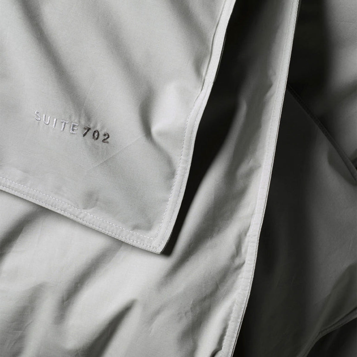 Nahaufnahme der Eckecke des Suite702 Perkal-Bettdeckenbezugs in Urban Grey mit Schriftzug „Suite702“