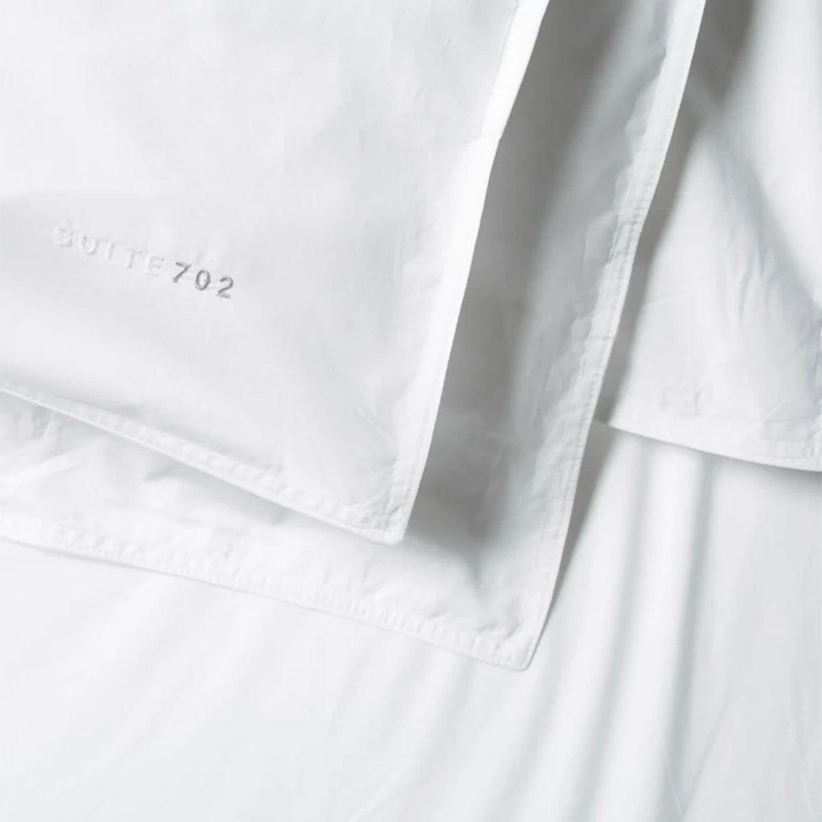 Nahaufnahme des Suite702 Perkal-Bettdeckenbezugs in Weiß mit eingesticktem „Suite702“-Schriftzug