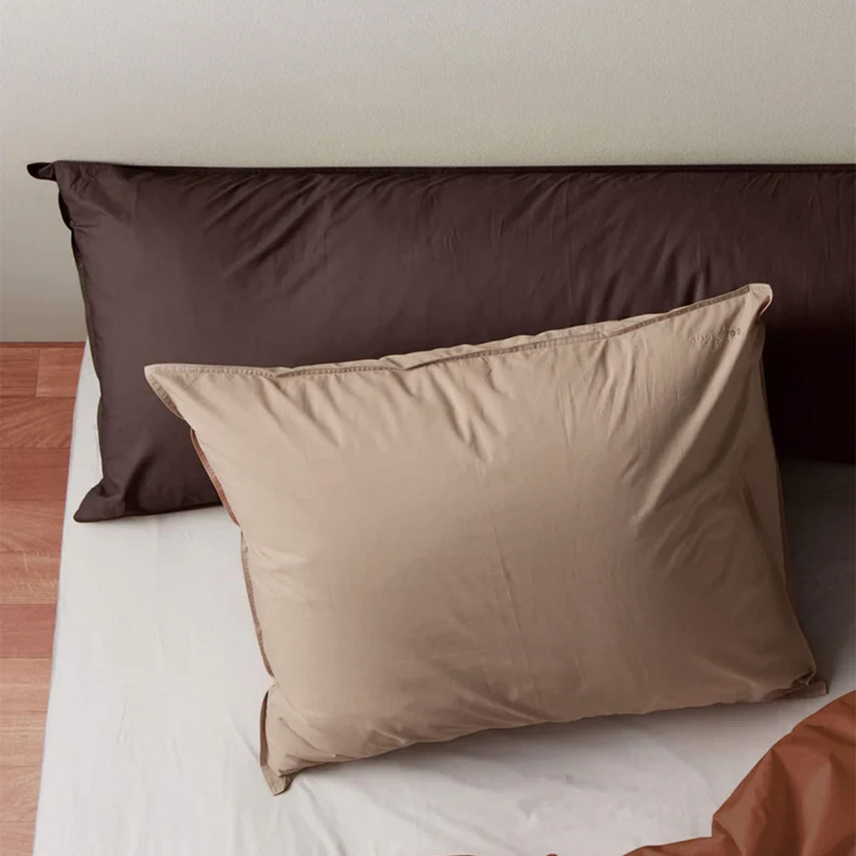 Suite702 Perkal Kissenbezug in Camel vor einem braunen Kopfteil-Kissenbezug im selben Design