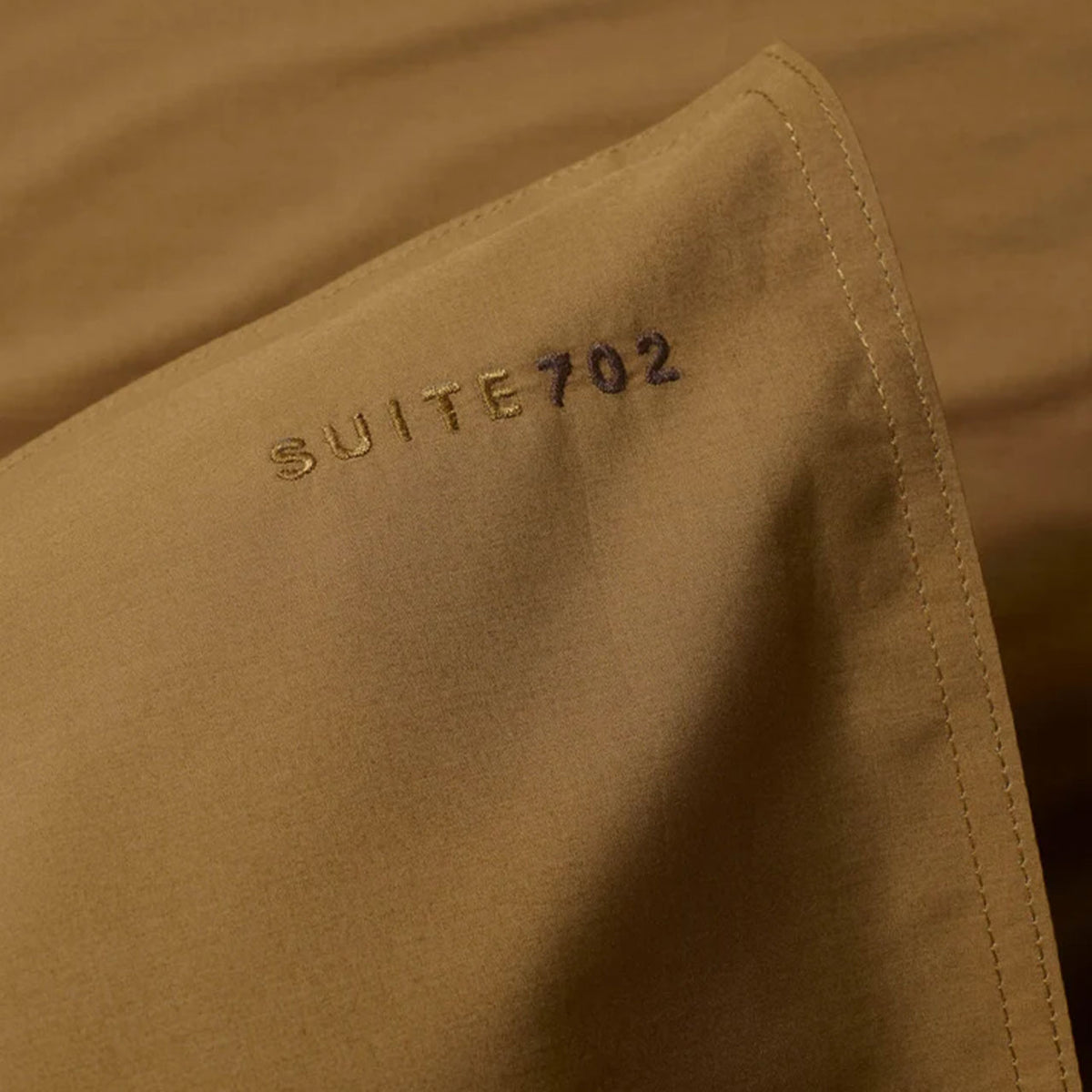 Nahaufnahme der Ecke eines Suite702 Perkal-Kissenbezugs in Khaki Gold mit „Suite702“-Schriftzug