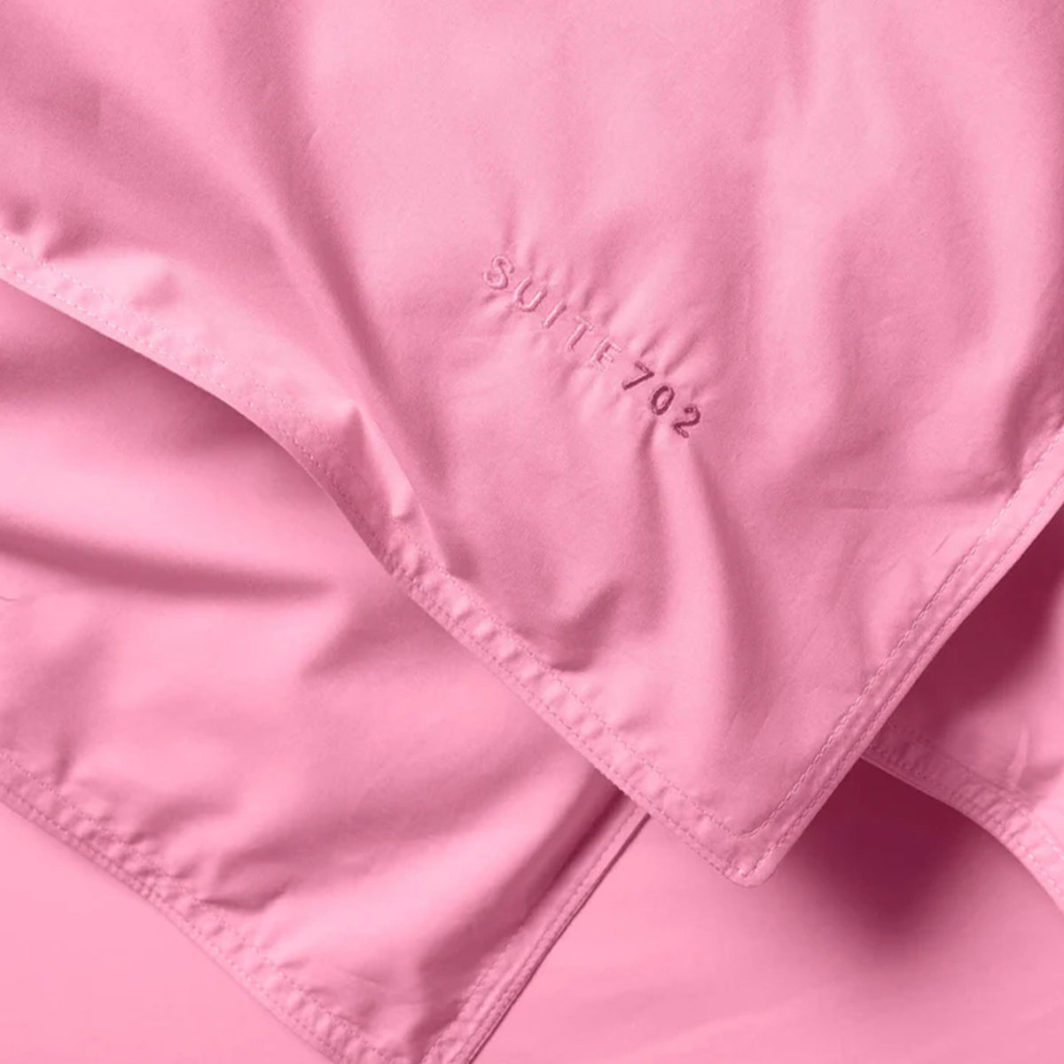 Nahaufnahme der Ecke des Suite702 Perkal Kissenbezugs in Pink mit gesticktem „Suite702“-Schriftzug