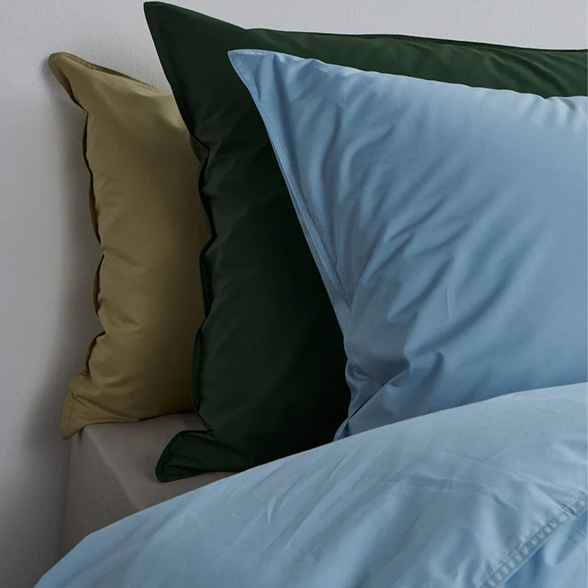 Suite702 Perkal Kissenbezüge in Sky Blue, Olive Green und Khaki Gold gestapelt auf Bett